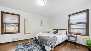 Ein Schlafzimmer mit einem Bett, einem Nachttisch, einem Spiegel und einem Fenster mit Jalousien.