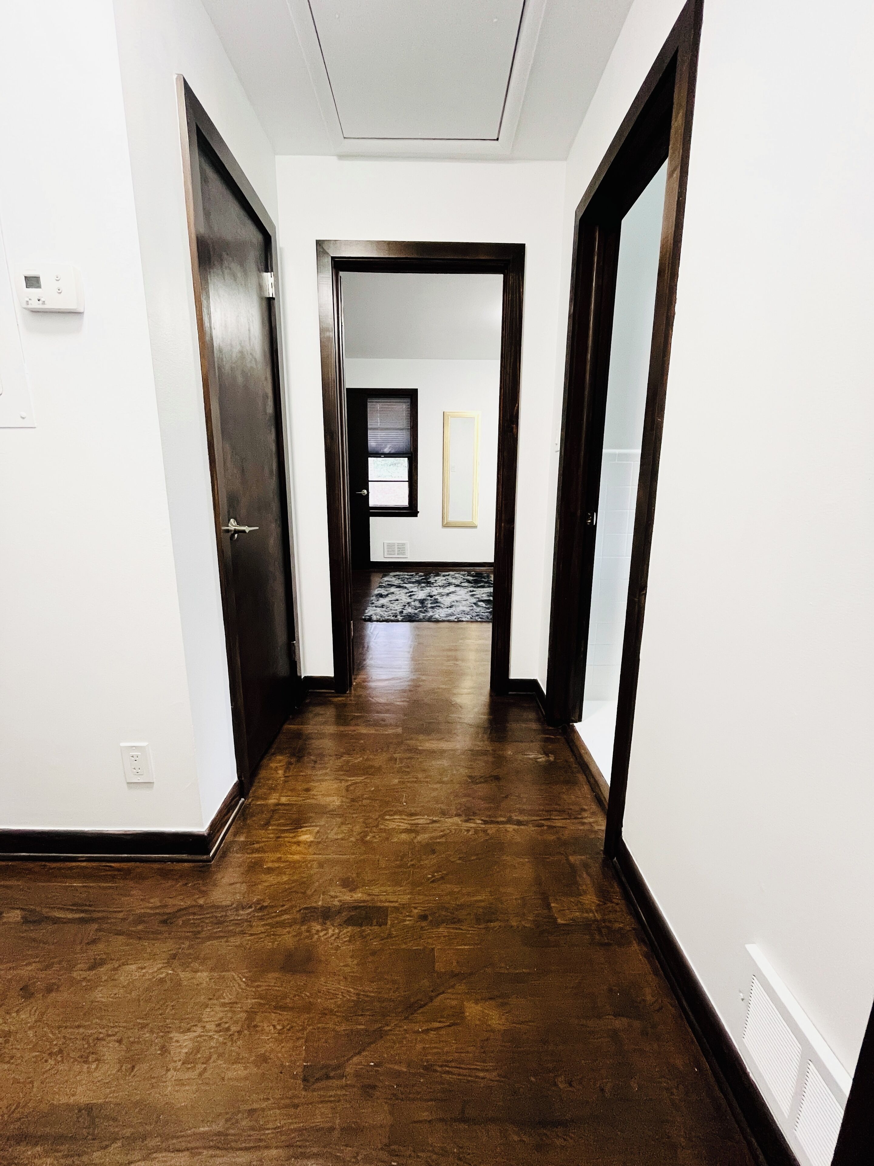 A hallway with wooden flooring, white walls, and a door at the end.