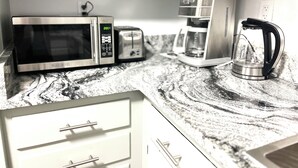 Eine Küche mit Mikrowelle, Toaster, Kaffeemaschine und Wasserkocher auf einer Marmorarbeitsplatte.