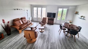 A modern living room with a brown leather sofa, a wooden coffee table, and a dining area with a round table and chairs.