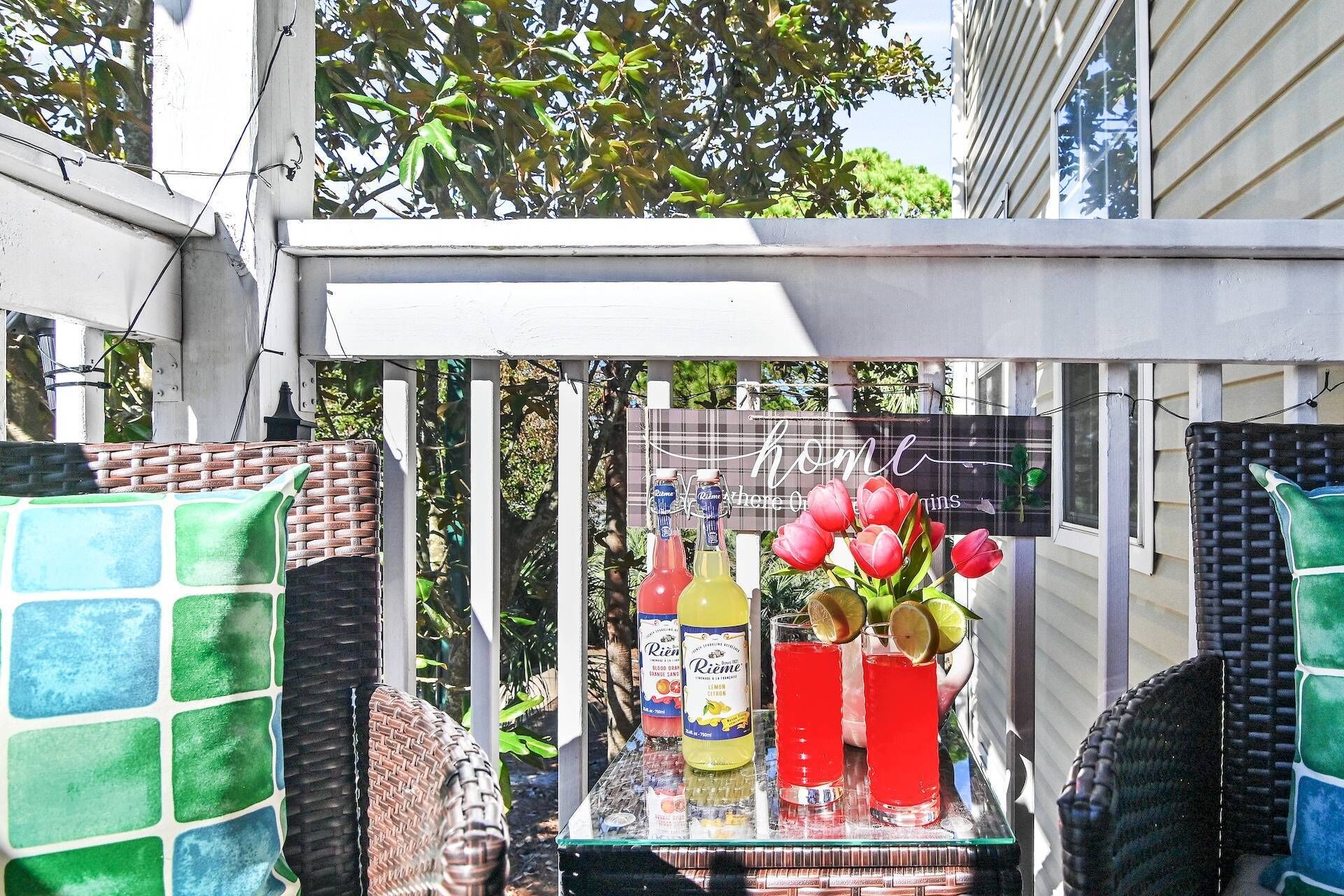 Una mesa de vidrio con botellas y un jarrón de flores rojas en un balcón.