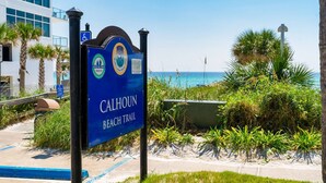 Opastekyltti, joka osoittaa Calhoun Beach -rantareitin, ja taustalla näkyy meri sekä rakennus.