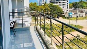 A balcony with a chair, a railing, and a view of buildings and greenery.