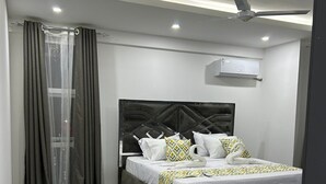 A modern bedroom with a large bed, grey curtains, a ceiling fan, and an air conditioning unit.