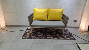 Um sofá cinzento com almofadas amarelas, um tapete estampado com flores e uma parede com textura.