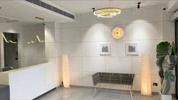 Uma área de recepção moderna com um balcão branco, um banco e uma grande planta em vaso.