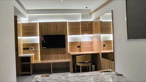 Quarto moderno com TV de tela plana na parede, painéis de madeira, um banco e uma pequena mesa com cadeiras.
