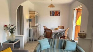 A cozy living room with a sofa, a dining area with a table and chairs, and a kitchen in the background. - Beautiful house with large spring-water pool at the gateway to the Cévennes  (Alès)