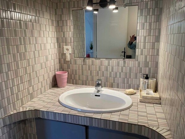 A bathroom with a white sink, a mirror, and a pink trash bin.
