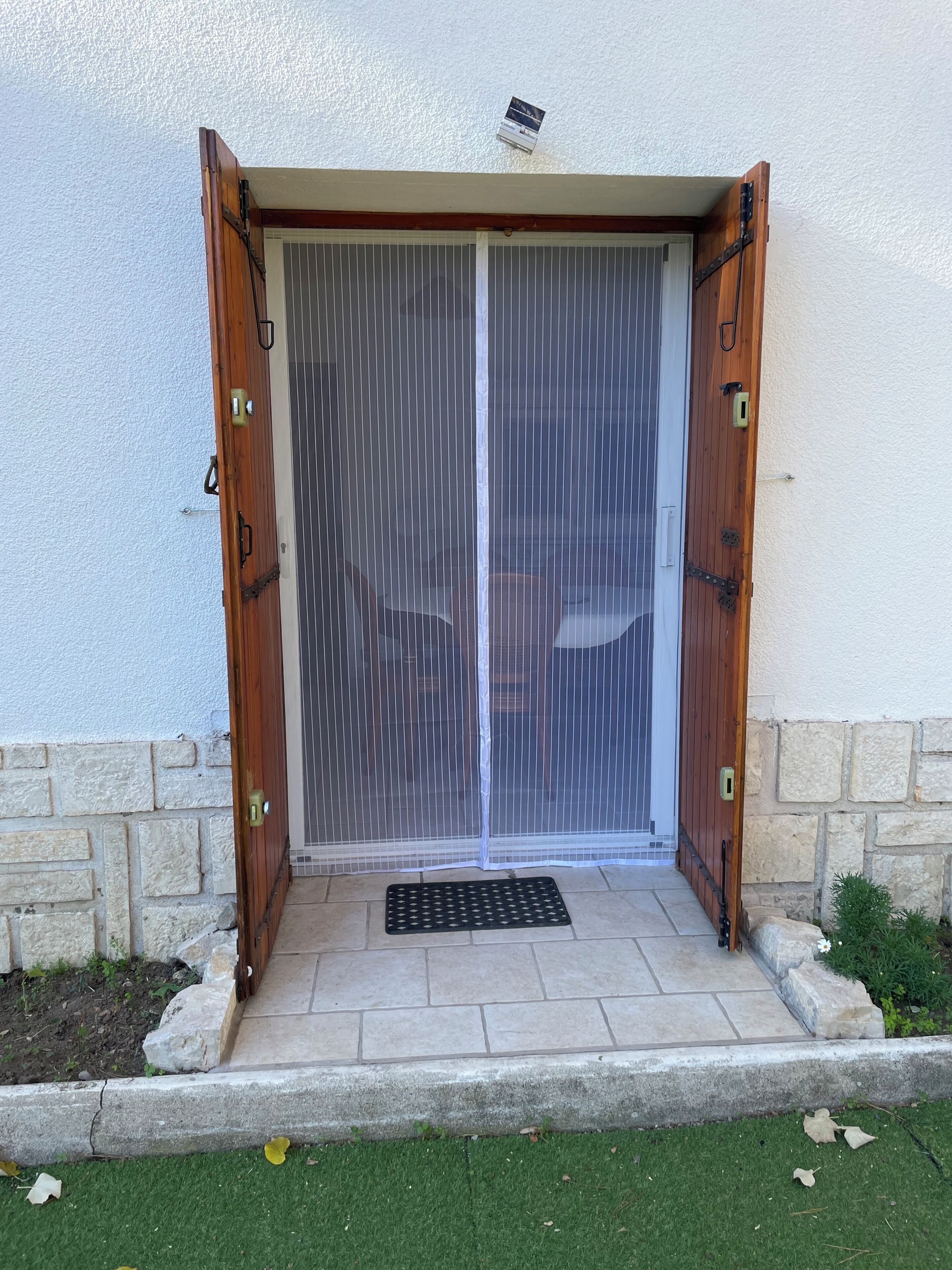 A sliding glass door with a metal security screen, a stone base, and a small garden area with a stone wall and greenery.