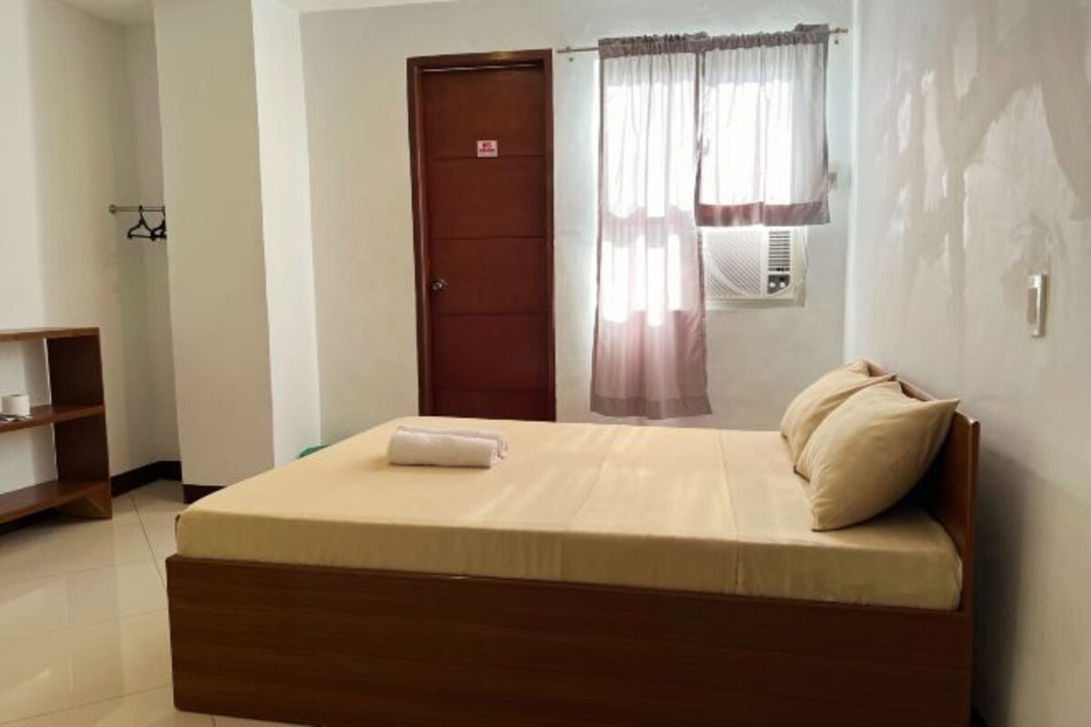 A bedroom with a wooden bed, a wardrobe, a hanging clothes rack, and a window with curtains.