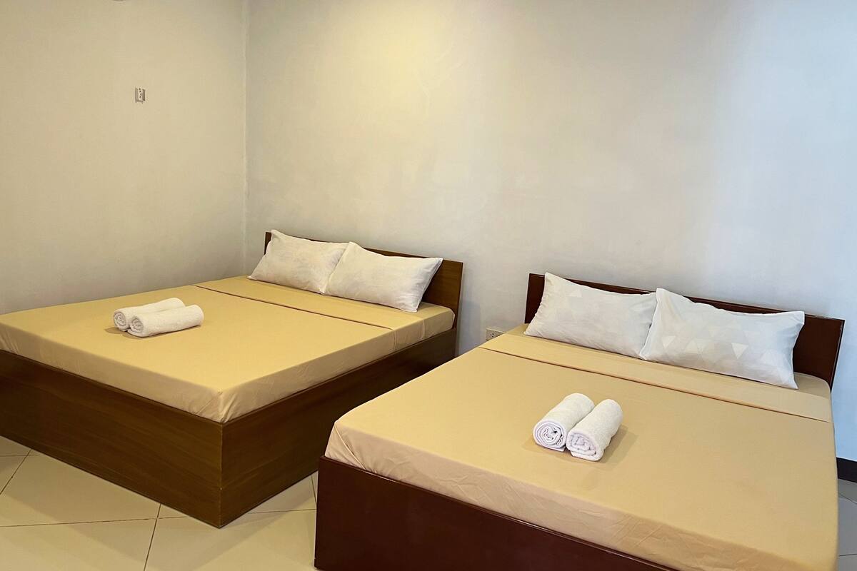 Two single beds with beige bedding and white pillows, each with a rolled white towel.