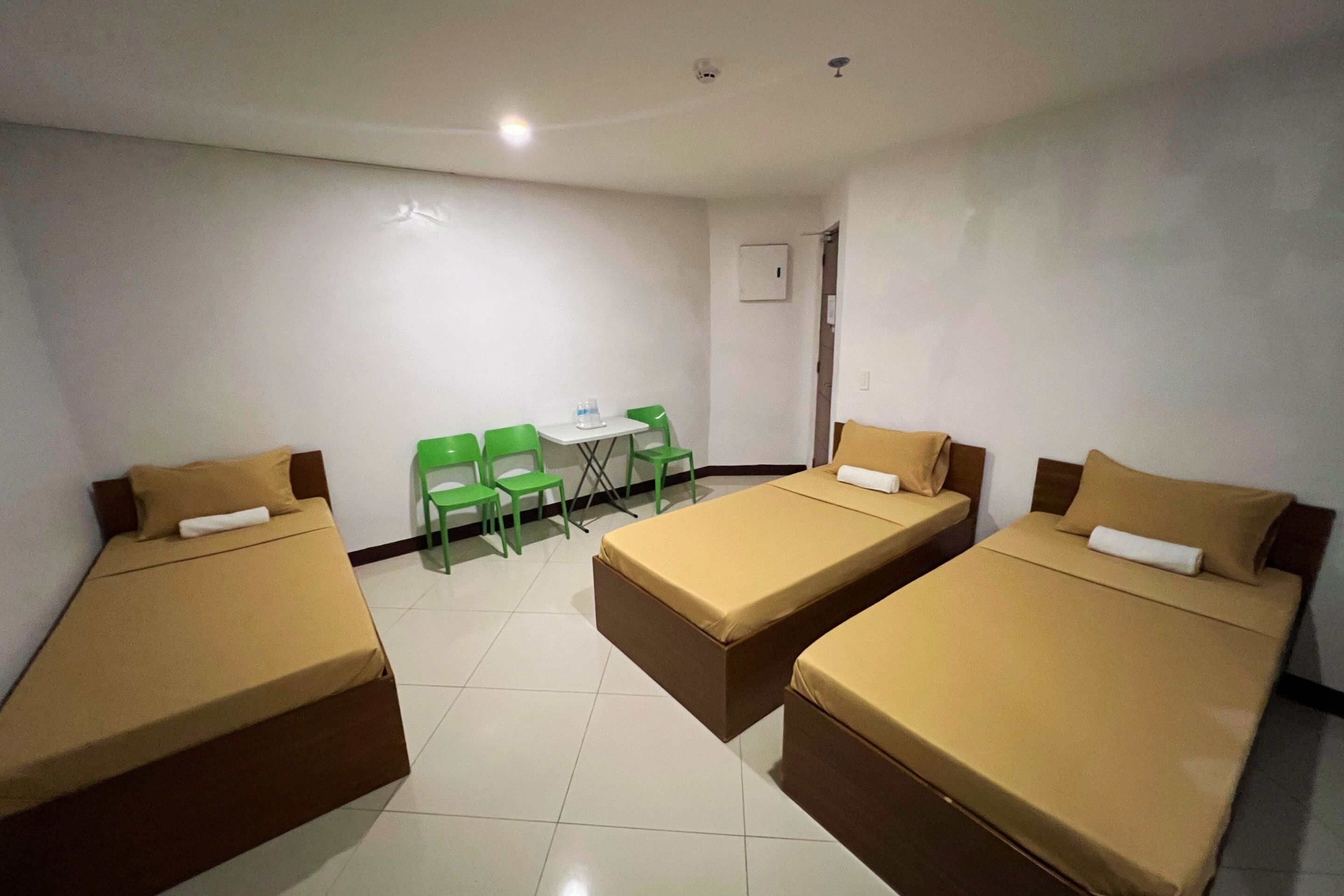 A room with three single beds, a small table, and two green chairs.