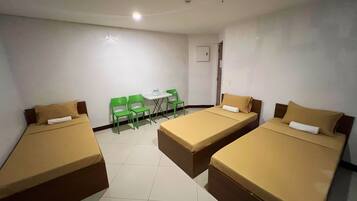 A room with three single beds, a small table, and two green chairs.