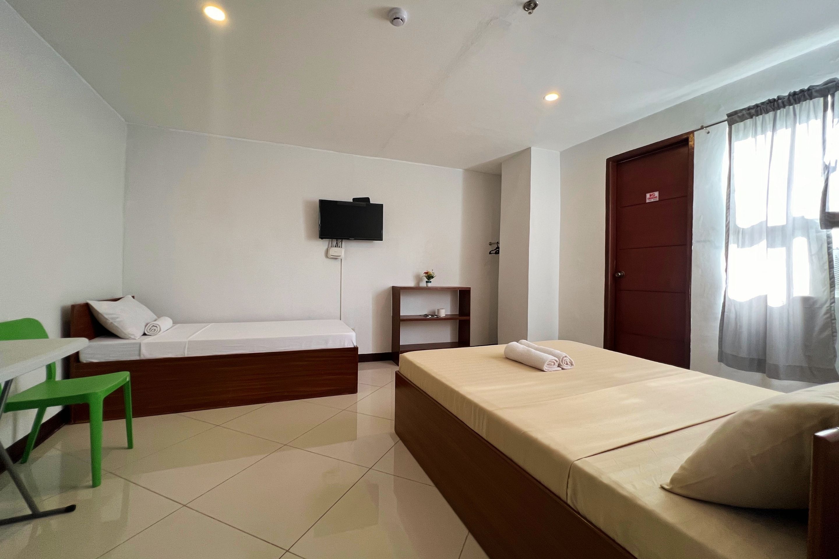 A hotel room with a bed, a desk, a chair, a TV mounted on the wall, and a door with a curtain.