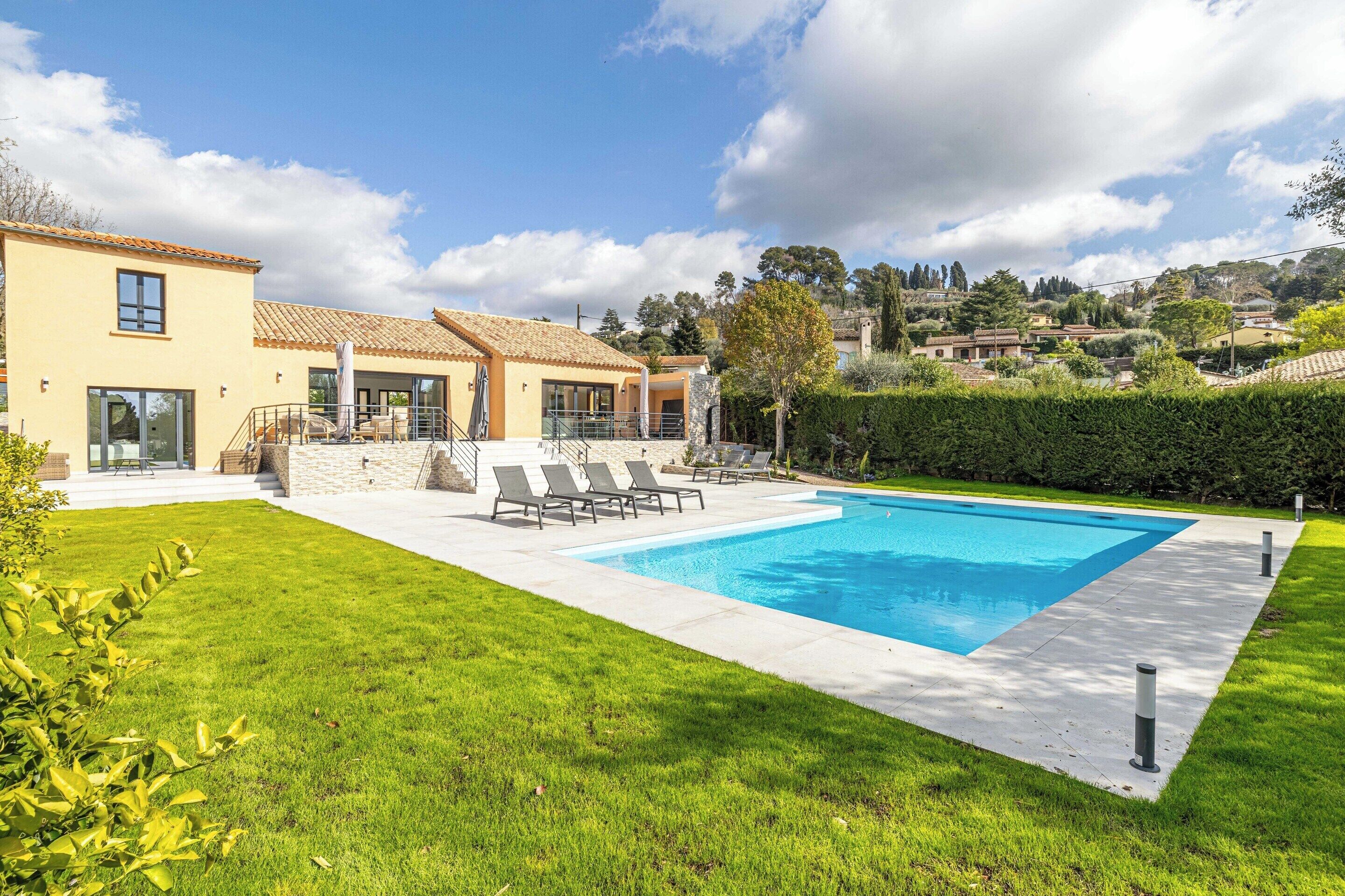 A modern house with a swimming pool, a patio with lounge chairs, and a well-maintained lawn.