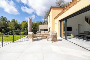 A modern outdoor patio with a sofa set, a dining table, and a glass-enclosed room.