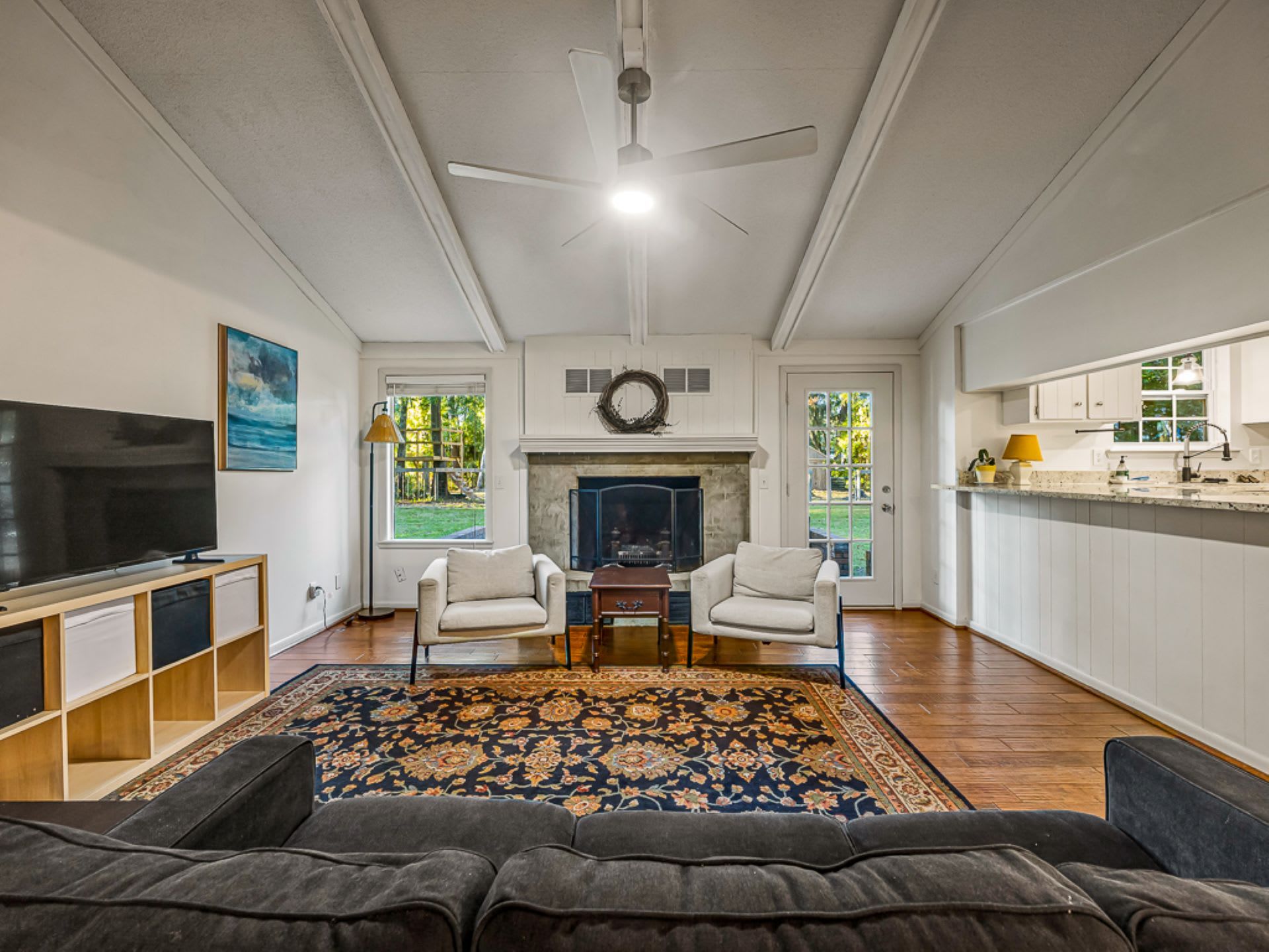 A living room with a television, two armchairs, a fireplace, and a large rug.