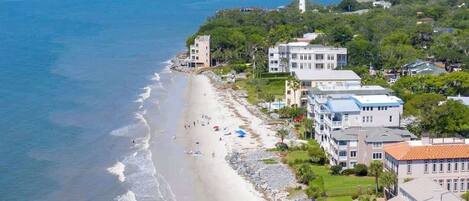 A coastal hotel with beachfront access, multiple buildings, and a lighthouse in the background.
