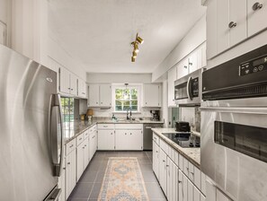 Una cocina moderna con armarios blancos, electrodomésticos de acero inoxidable, una isla central y una alfombra estampada.