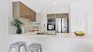 A modern kitchen with stainless steel appliances, wooden cabinets, and a white countertop. - Chic Coastal Charm on Palm Beach (Palm Beach)