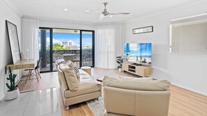 A modern living room with a sofa, a coffee table, and a TV. There is a balcony with a view of the city. - Chic Coastal Charm on Palm Beach (Palm Beach)