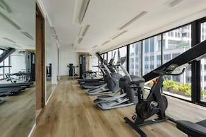 A gym with exercise equipment, large windows, and a wooden floor.