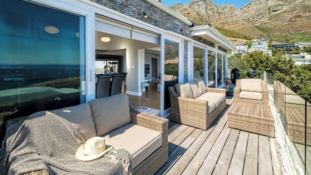 A covered outdoor area with wicker furniture, a dining area, and a view of the mountains. - Stylish Camps Bay Home with Sea Views Beleza Villa (Cape Town)