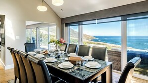 A dining area with a table set for four, large windows offering a view of the ocean, and pendant lighting. - Stylish Camps Bay Home with Sea Views Beleza Villa (Cape Town)
