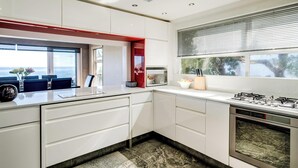 A modern kitchen with white cabinetry, a gas stove, a microwave, and a window with blinds. - Stylish Camps Bay Home with Sea Views Beleza Villa (Cape Town)