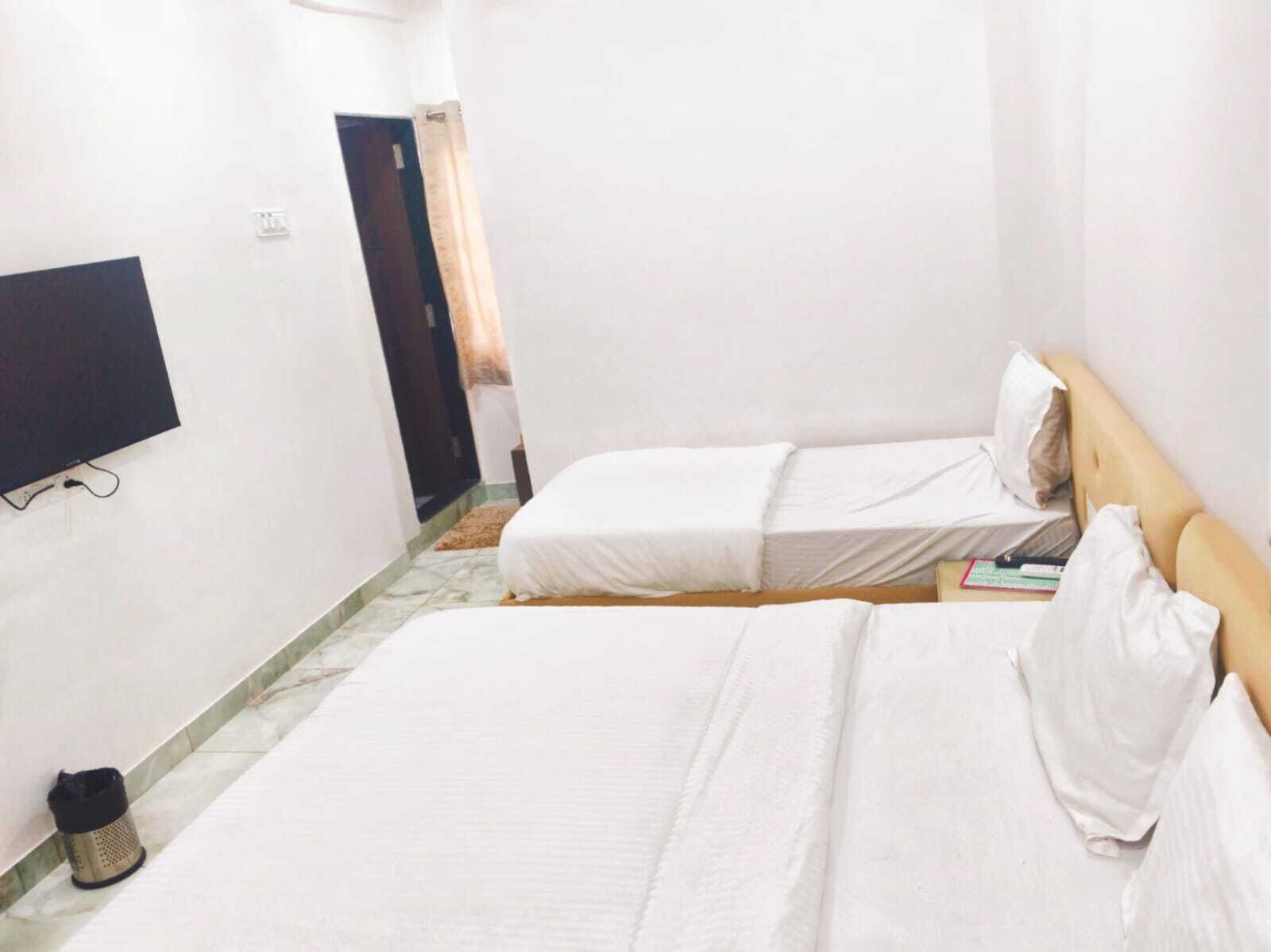 Quarto com duas camas, televisão na parede e uma lixeira.