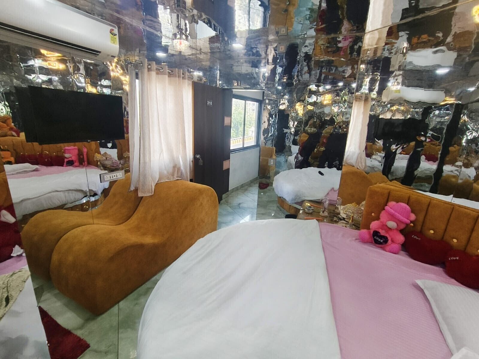 A hotel room with a large mirror, a bed, a brown armchair, and a pink stuffed toy.