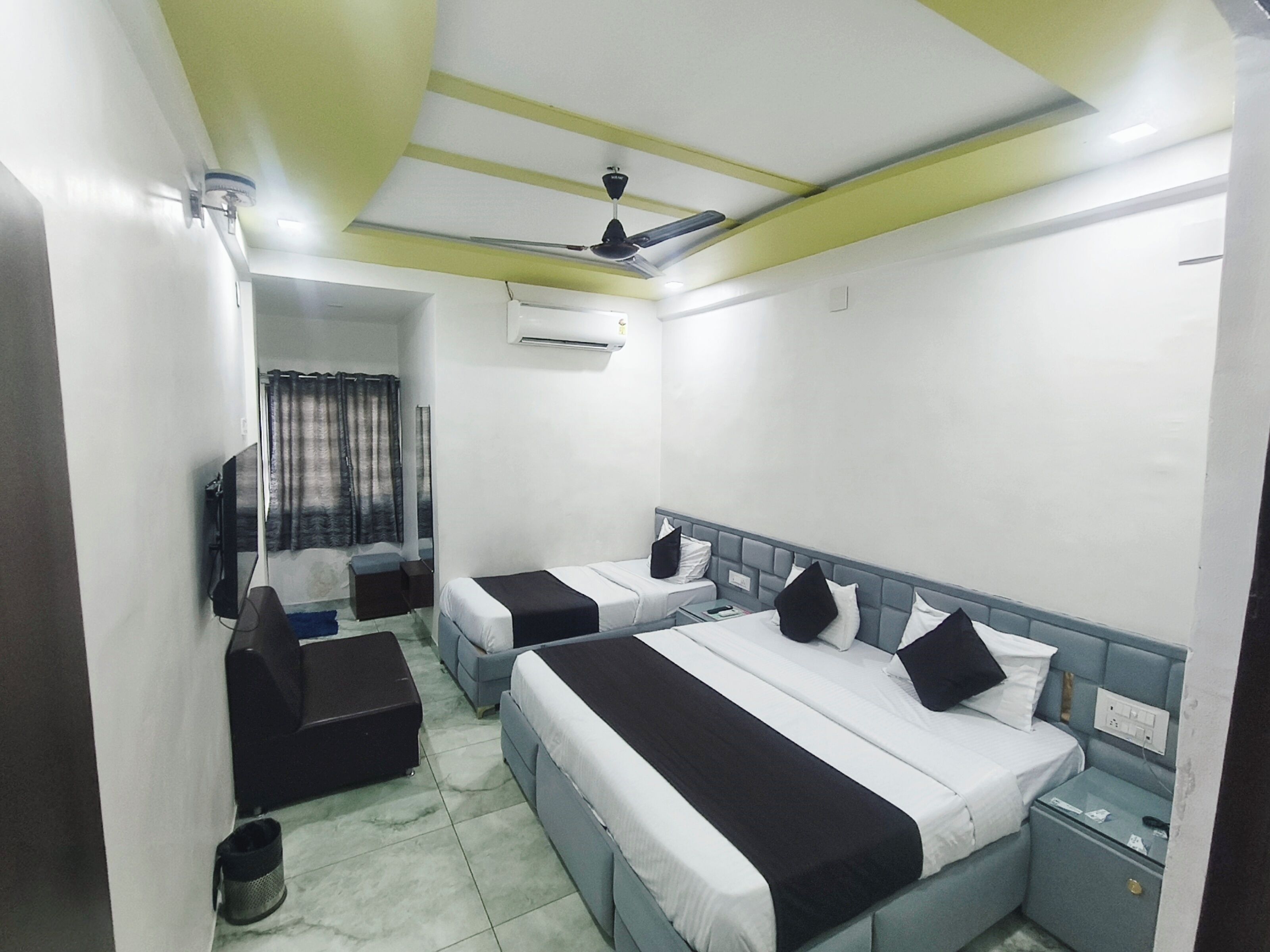 Habitación de hotel con dos camas, ventilador de techo, aire acondicionado, una mesita y una silla.