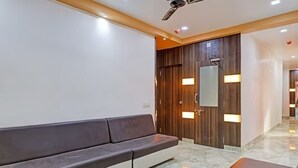Eine moderne Hotelhalle mit einem dunkelbraunen Sofa, einer Holztür mit beleuchteten Feldern und einem Deckenventilator.