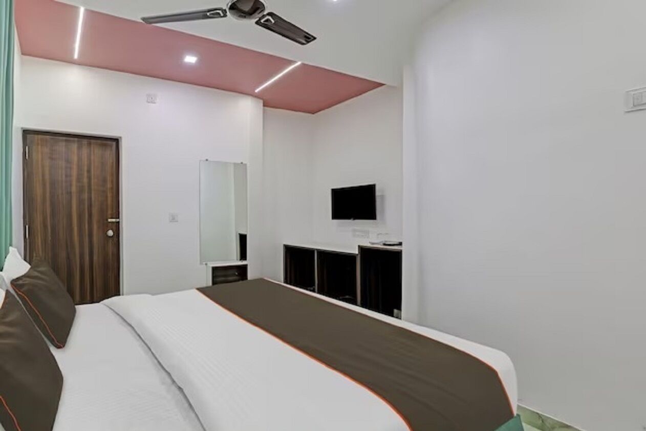 A modern hotel room with a large bed, a flat-screen TV, a wardrobe, and a desk.