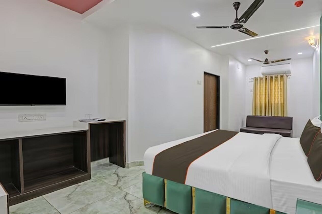 Een moderne hotelkamer met een flatscreen televisie, een bed met een groen en wit hoofdeinde, en een plafondventilator.