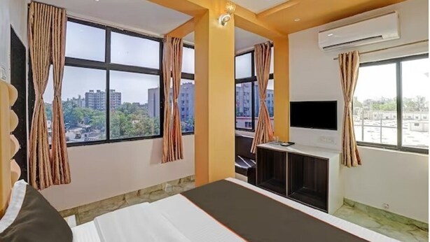 Ein Hotelzimmer mit Bett, Schreibtisch, Fernseher und großen Fenstern mit Vorhängen.