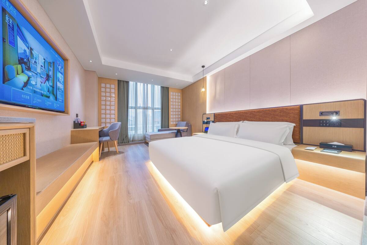 A modern hotel room with a large bed, a desk, a chair, and a TV mounted on the wall.