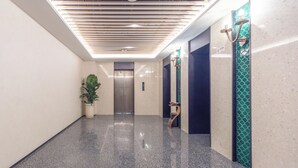 A modern hallway with a polished floor, a potted plant, an elevator, and decorative wall panels. - True Go S Hotel Nanshan Nantou (Shenzhen)