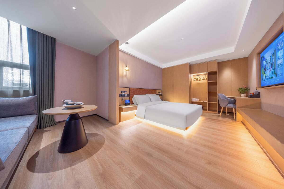 A modern hotel room with a bed, a round table, a desk, and a sofa.