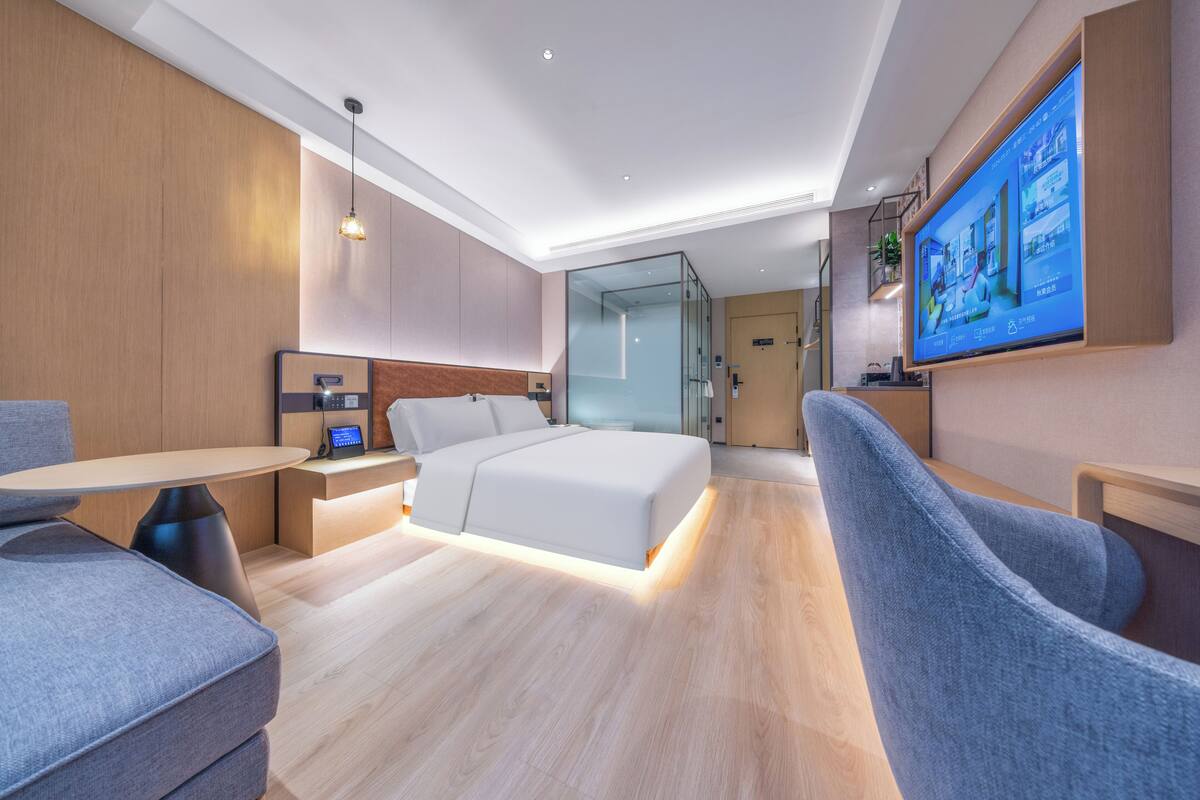 A modern hotel room with a bed, a desk, a chair, a TV, and a glass partition.
