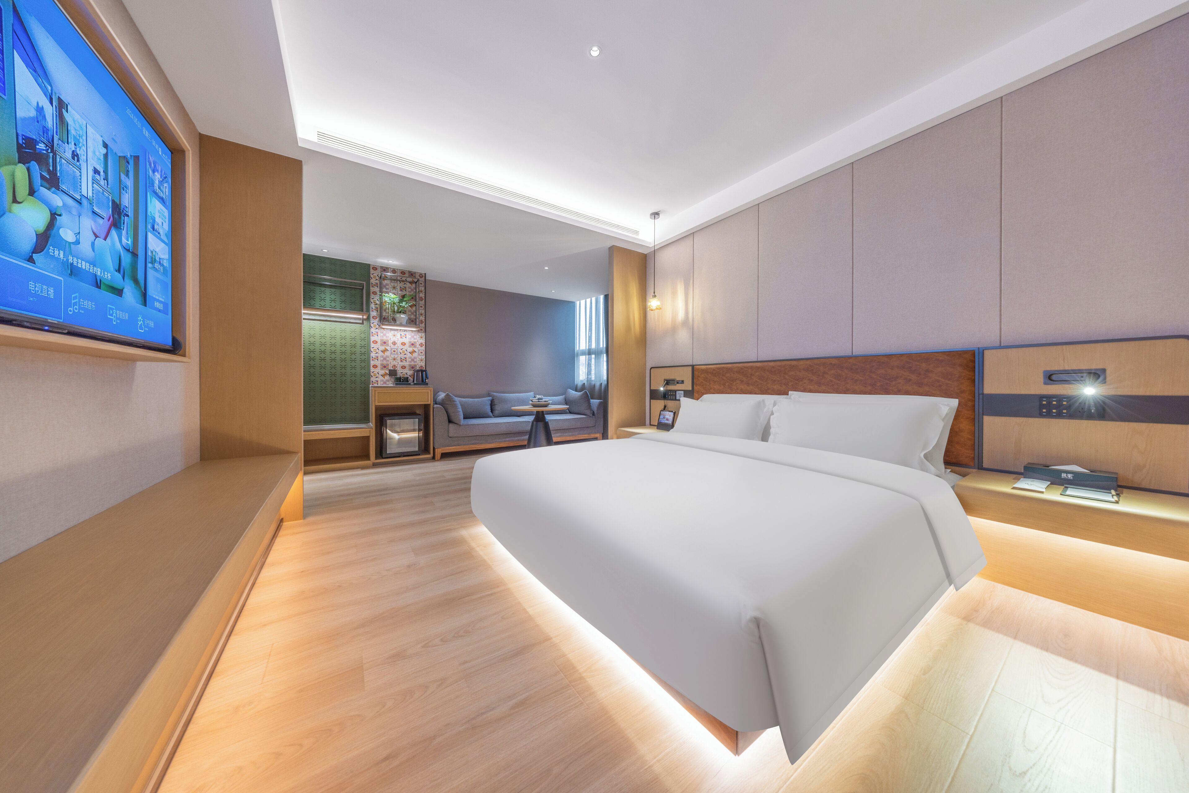 Una camera d'albergo moderna con un letto grande, una TV fissata al muro, un divano e un tavolino.
