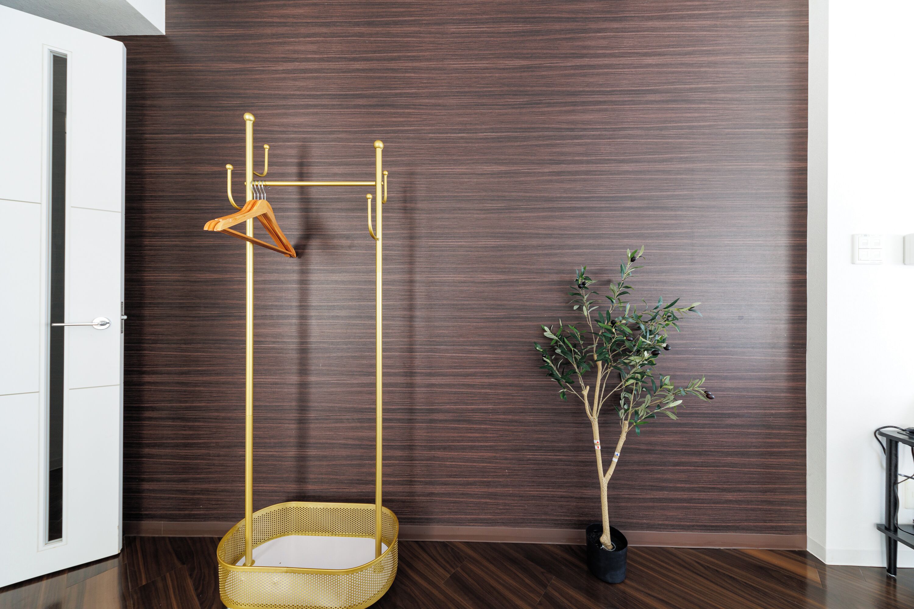 Una habitación con una pared de madera oscura, un perchero de madera colgante, una cesta de mimbre y una planta en maceta.