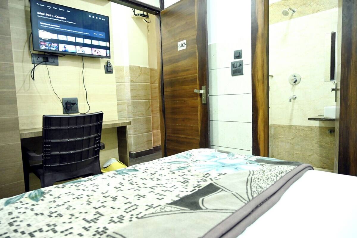 Una habitación de hotel con una cama, un escritorio, un televisor montado en la pared y una puerta de madera con el número 302.