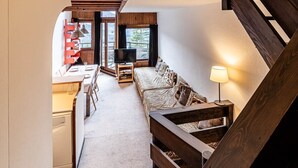 Un intérieur moderne avec un escalier en bois, un coin repas doté d’un téléviseur et un canapé avec une lampe.