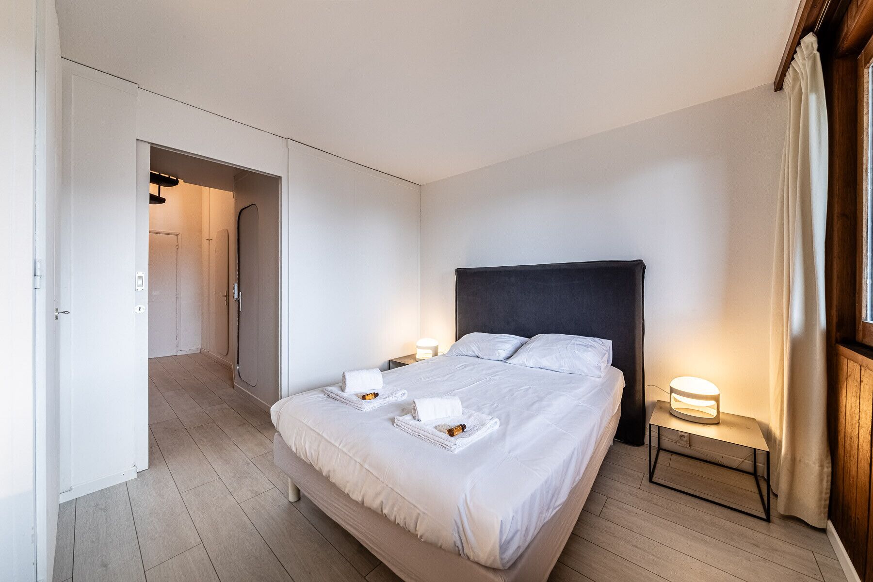 A hotel room with a bed, bedside tables, and a door leading to another room.