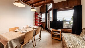 Un salon chaleureux avec une table à manger en bois, mise pour deux personnes, un téléviseur et une bibliothèque.
