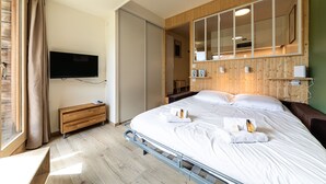 Ein modernes Hotelzimmer mit Bett, Fernseher, Holzschrank und großem Spiegel.