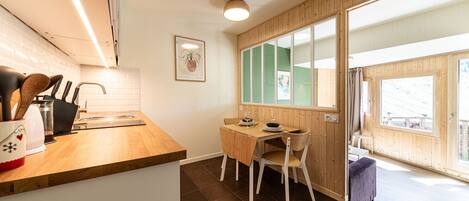 A compact kitchen with a wooden countertop, a dining area with a table and chairs, and a large window providing natural light.