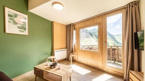 Ein Zimmer mit Holztisch, einem gerahmten Bild an der Wand und einem Fenster mit Blick auf die Berge.